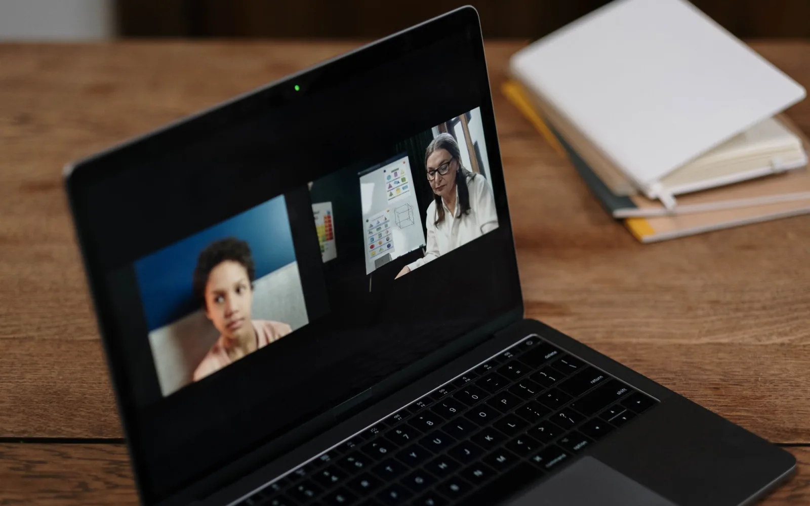 Twee leerlingen aan een tafel voor een laptop met een instructeur die op het whiteboard tekent — online klaslokaal.