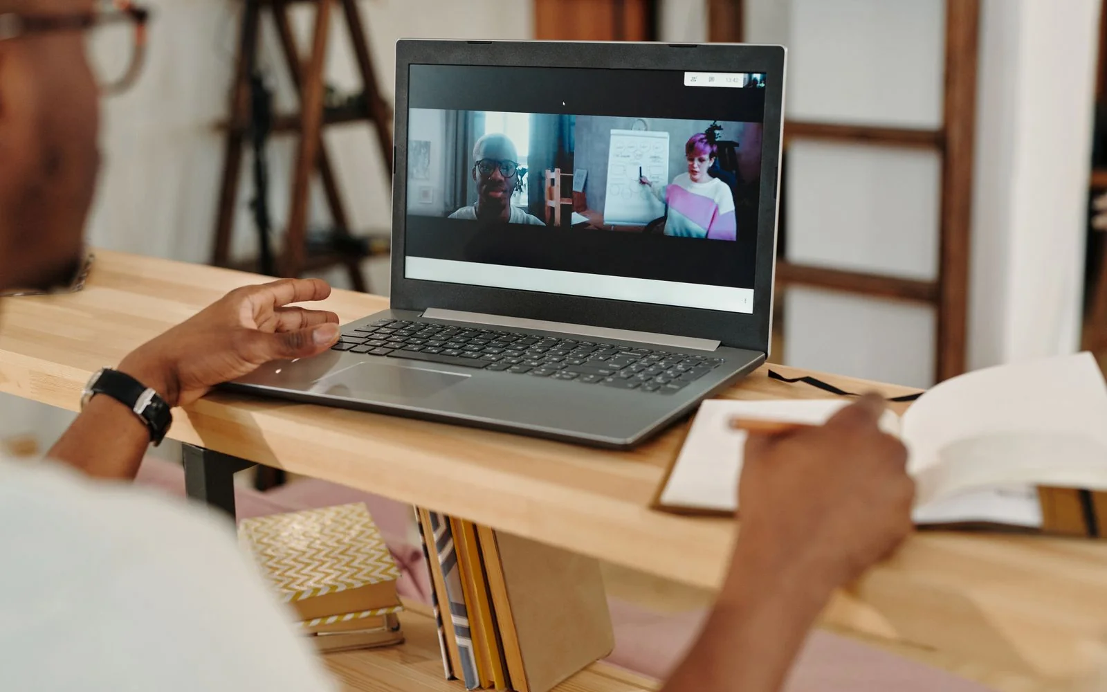 Vrouw achter haar laptop die aantekeningen maakt tijdens een webinar; op haar scherm een presentator en een rij deelnemer-tegels.